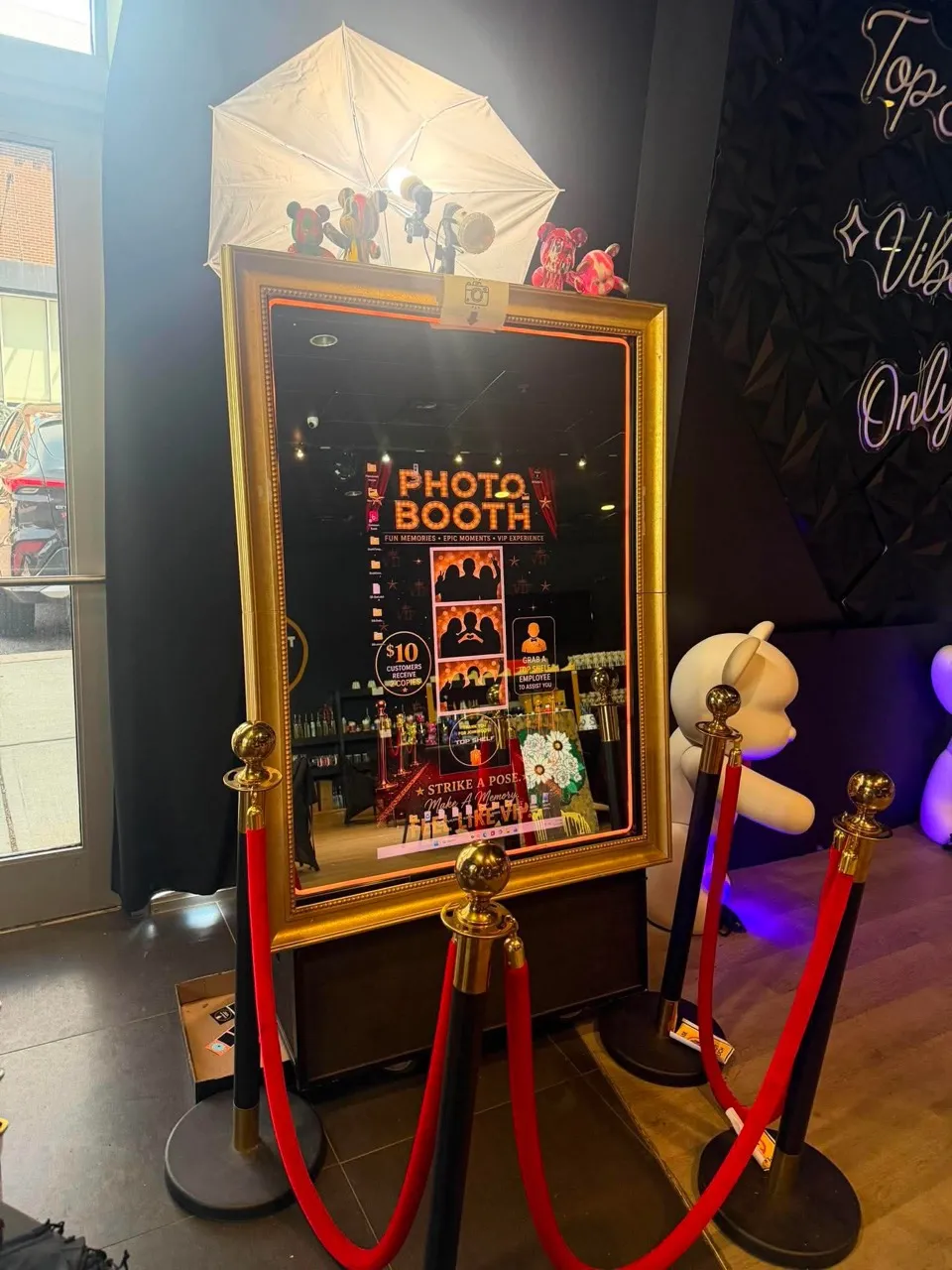 Gold-framed Magic Mirror photobooth camera setup with red and black stanchions
